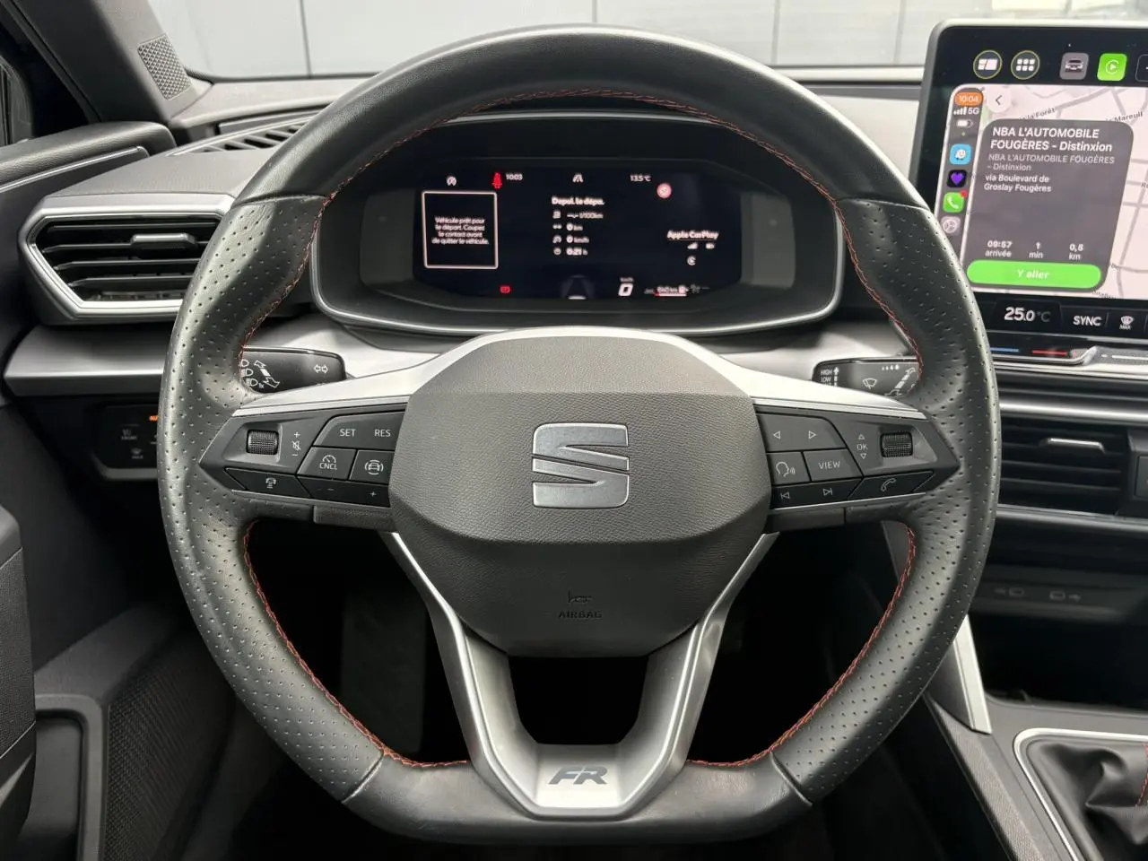 Vue rapprochée du volant en cuir noir avec surpiqûres rouges et tableau de bord numérique du SEAT Leon 1.5 e-TSI FR 2025.