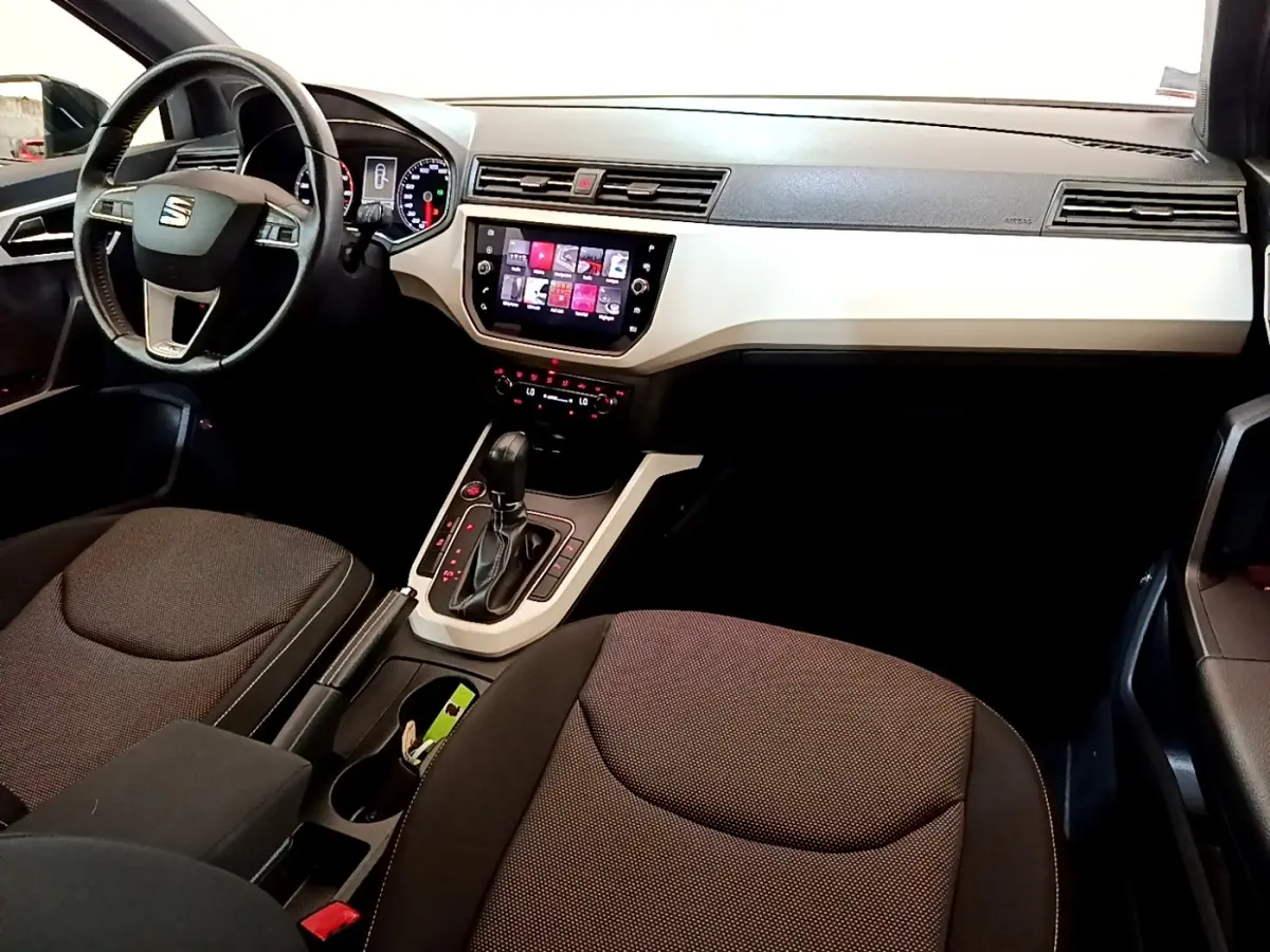 Vue intérieure avant droite du SEAT Arona gris clair 2019, volant cuir alu et écran tactile central visible.