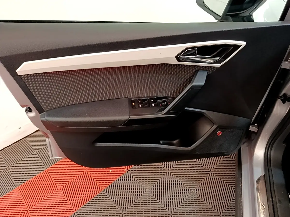 Vue latérale du panneau de porte avant gauche gris clair de la SEAT ARONA avec commandes de vitres et poignée chromée.