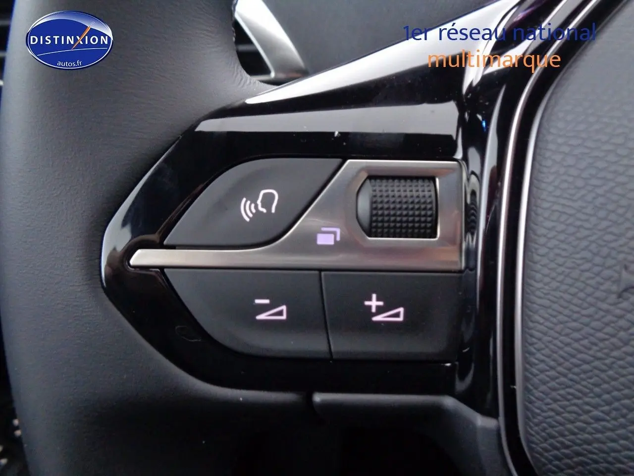 Gros plan sur les commandes de volume et de reconnaissance vocale sur le volant noir brillant d'une Peugeot 3008 2023.