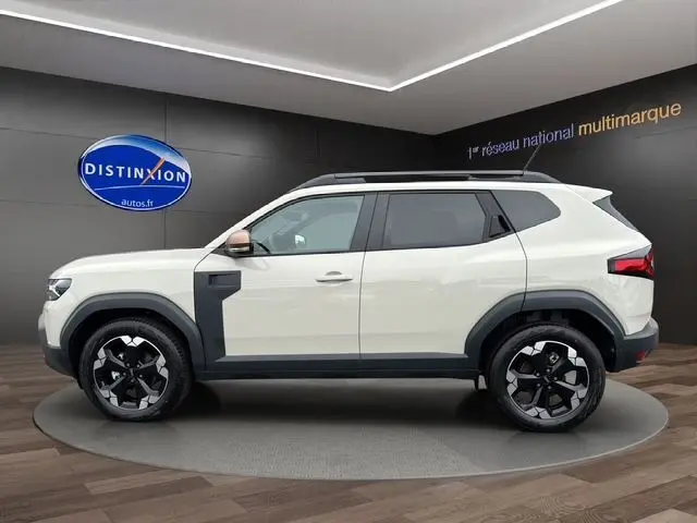 Profil côté gauche du Dacia Duster 2025 blanc avec jantes alu 18 pouces et protections noires contrastées.