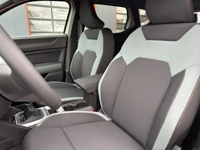 Vue intérieure des sièges avant gris clair et foncé du Dacia Duster 2025, avec accoudoir central et volant partiel visible.