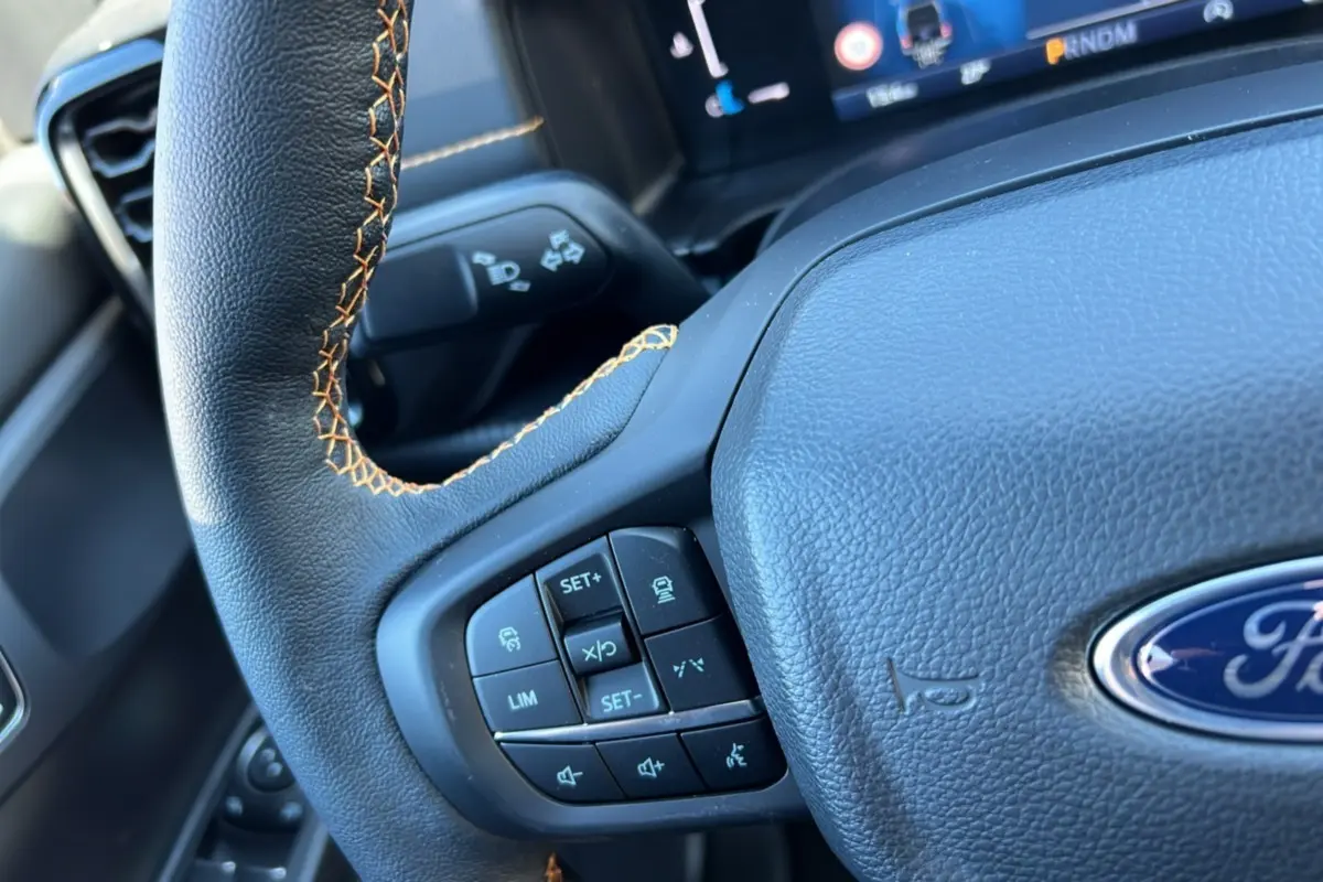 Gros plan sur le volant noir avec surpiqûres orange du Ford Ranger 2025, mettant en valeur les commandes multifonctions à gauche.