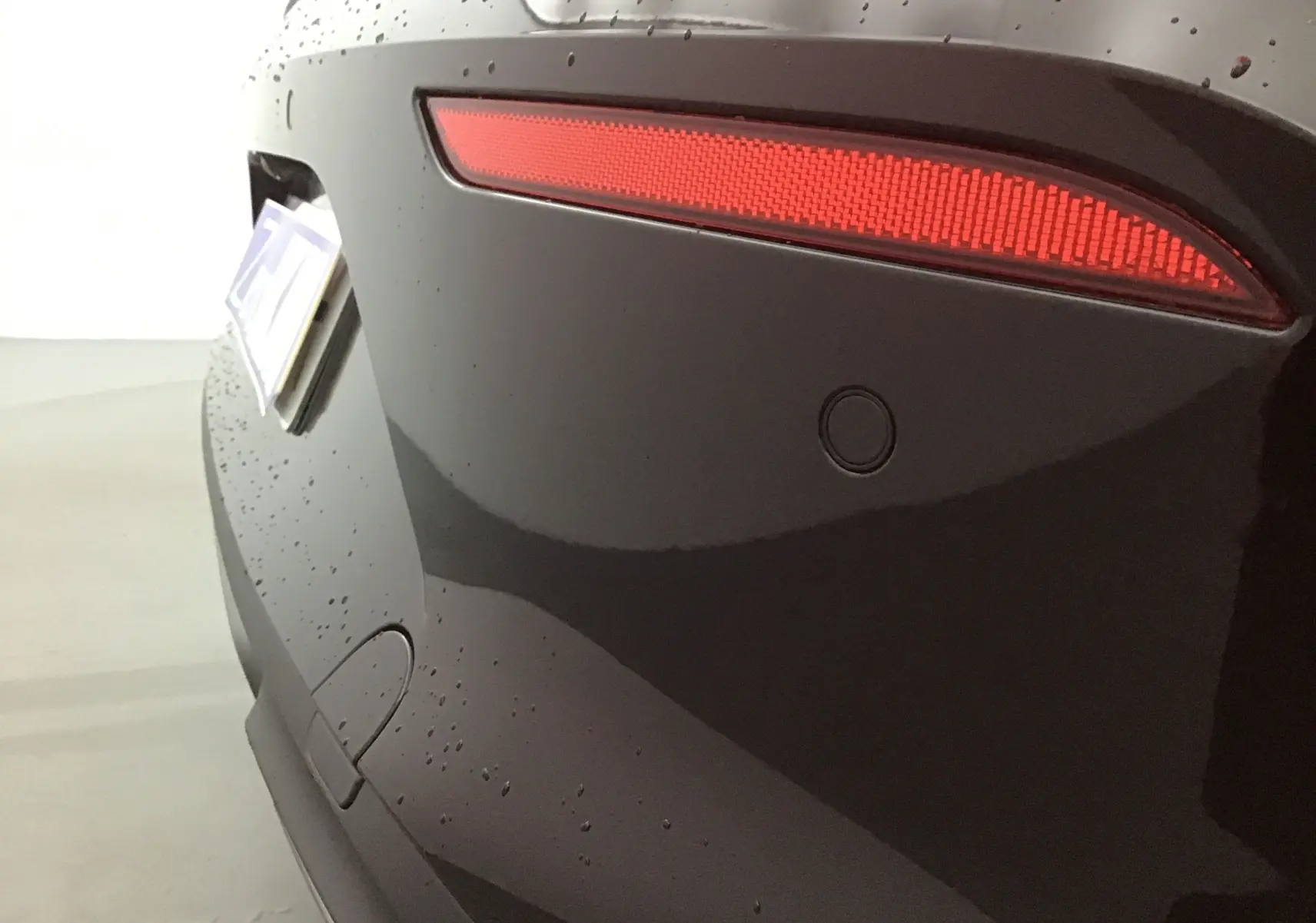 Gros plan sur le feu arrière droit rouge et la carrosserie noire brillante d'une CUPRA Leon 2023 sous la pluie.