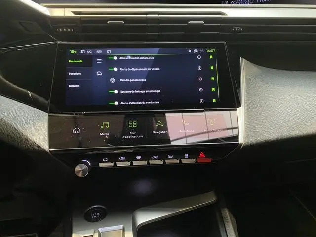 Vue rapprochée de l’écran tactile central et de la console de la Peugeot 308 hybride blanche, affichant les aides à la conduite.