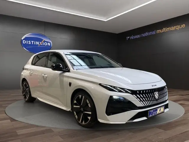 Vue 3/4 avant droite de la Peugeot 308 blanche Okenite, hybride, avec calandre distinctive et jantes noires bicolores.