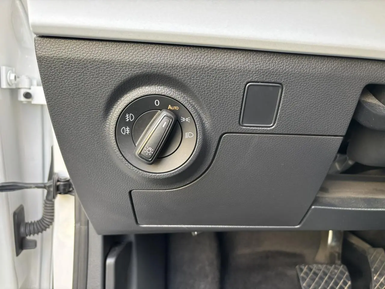 Gros plan sur le bouton de commande des phares à gauche du tableau de bord d'un SEAT Arona blanc, intérieur noir.