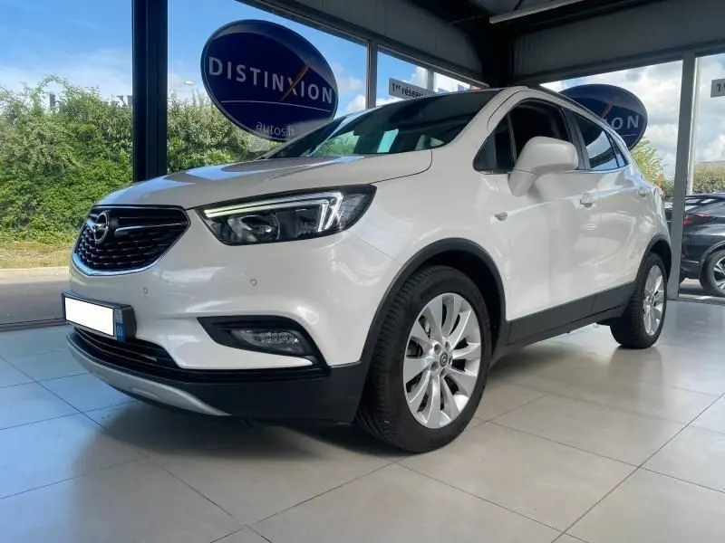 Opel Mokka blanc vue 3/4 avant droit en intérieur, avec calandre noire et jantes argentées multi-branches.