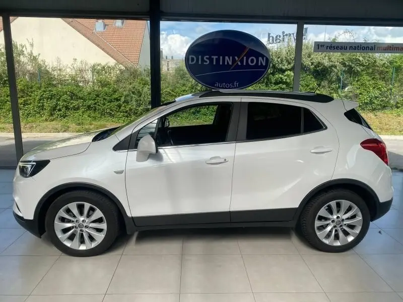 Opel Mokka blanc vu de profil côté gauche, montrant ses jantes alliage et ses lignes compactes en intérieur showroom.