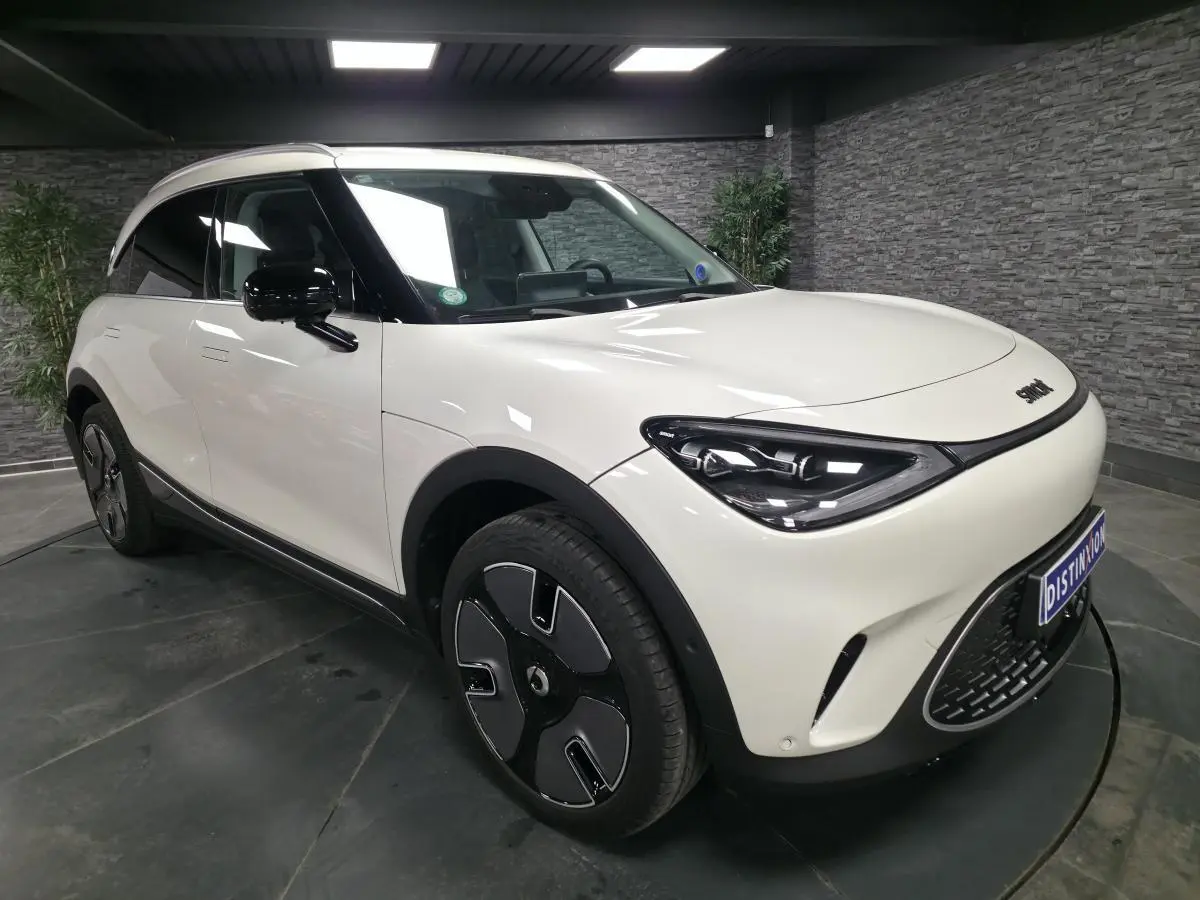 Vue 3/4 avant gauche d'une Smart #1 électrique blanche avec jantes noires et toit panoramique en verre.