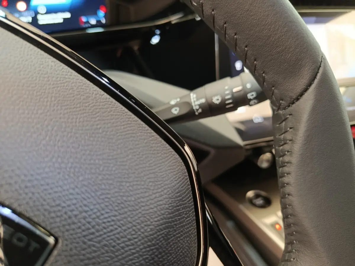 Gros plan sur le volant cuir multifonctions gris foncé de la Peugeot 308 2026, avec commandes intégrées et tableau de bord flou.