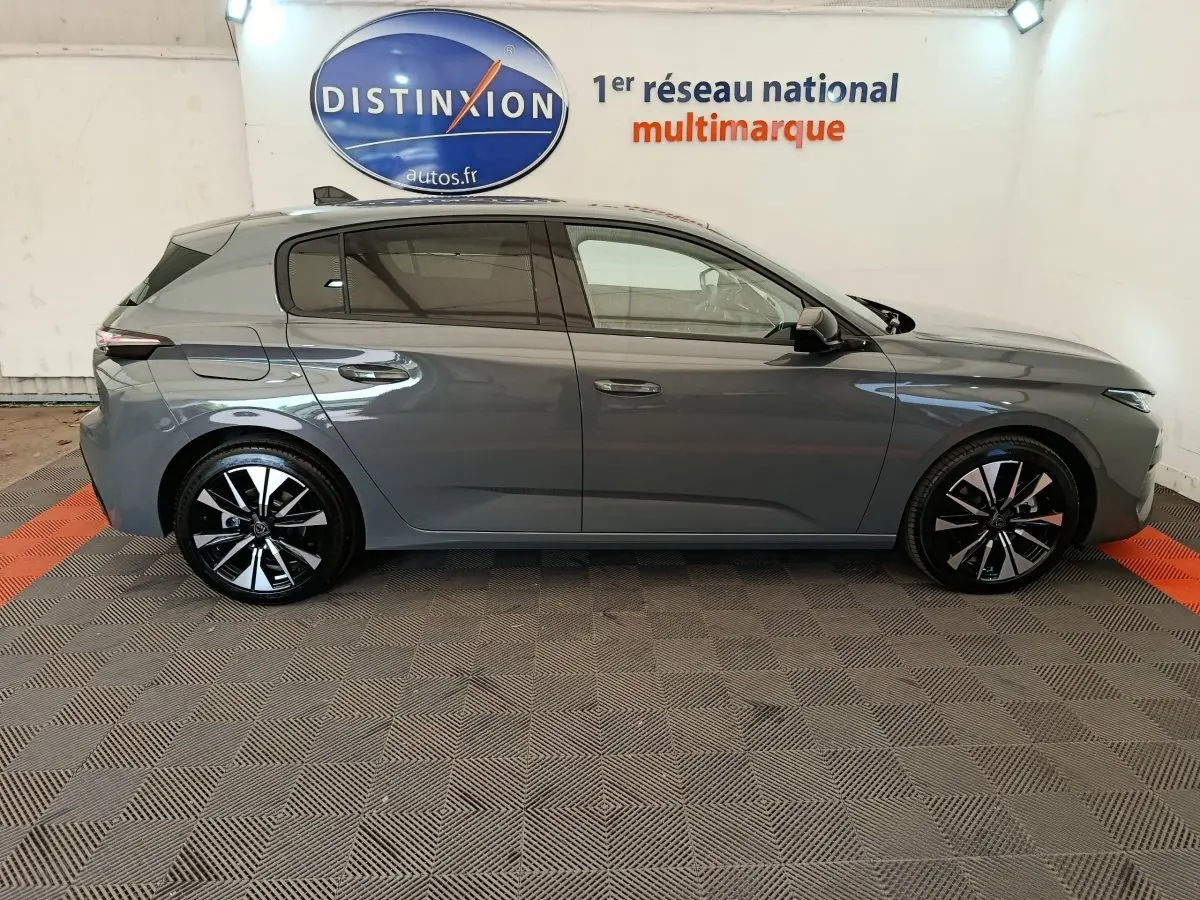 Profil côté droit d'une Peugeot 308 gris foncé 2026 avec jantes noires et détails chromés, en intérieur showroom.
