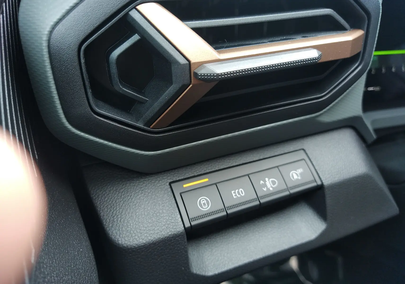 Gros plan sur la commande ECO et les boutons de réglage sous la sortie d'air au design hexagonal cuivré du tableau de bord Dacia Bigster.