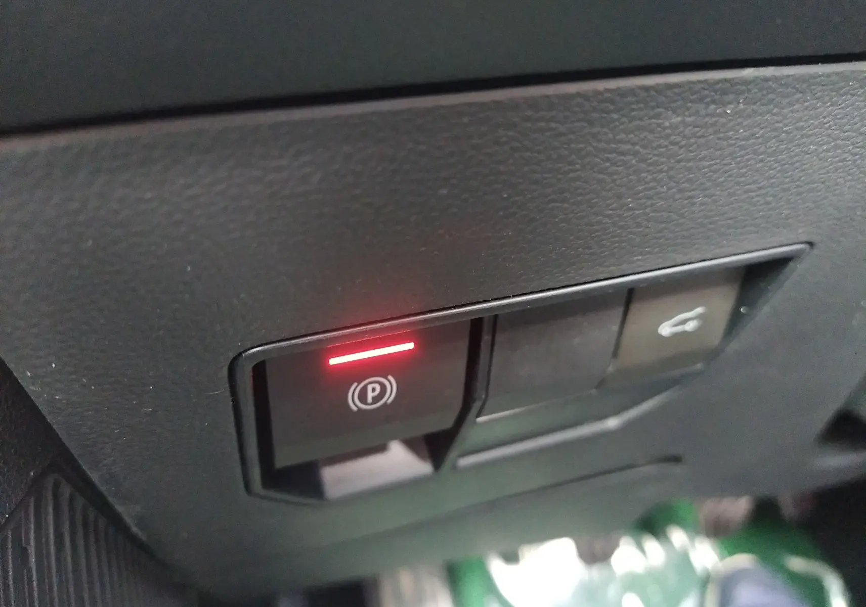 Gros plan sur le bouton de frein à main électronique allumé dans l'habitacle du Dacia Bigster gris schiste.