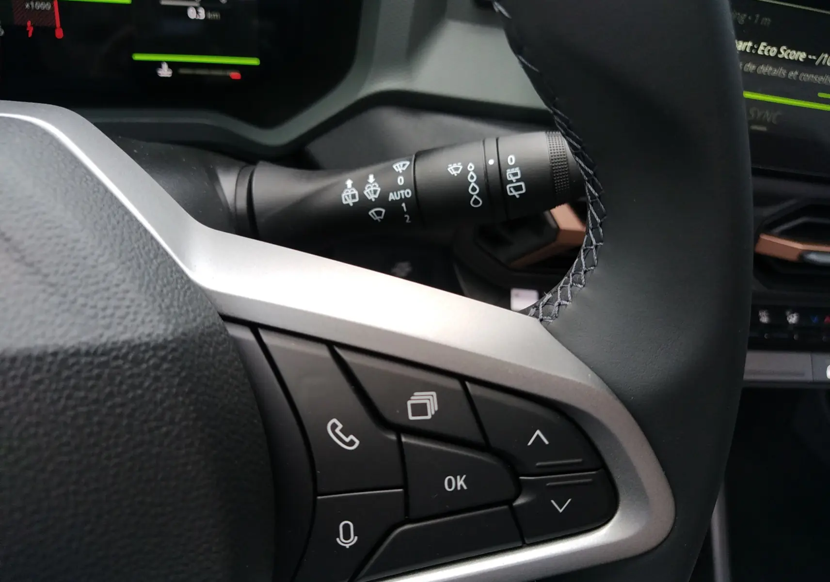 Gros plan sur le volant noir et gris du Dacia Bigster 2025, avec commandes multifonctions et manette d'essuie-glace visible.