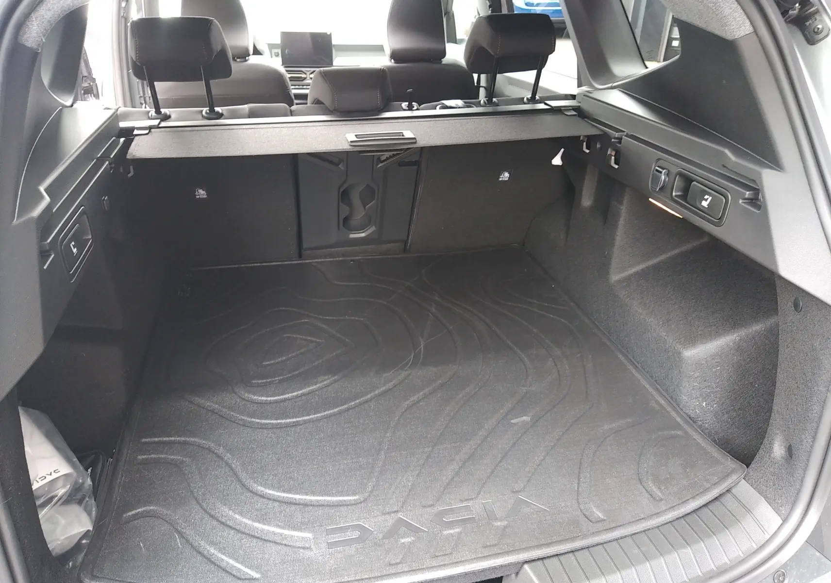 Coffre ouvert du Dacia Bigster gris schiste, vue arrière montrant un tapis de coffre avec logo et banquette arrière rabattue.