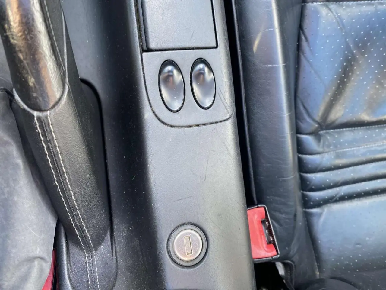 Gros plan sur la console centrale noire et le siège en cuir perforé côté conducteur d'une Porsche 911 Targa gris foncé 2004.