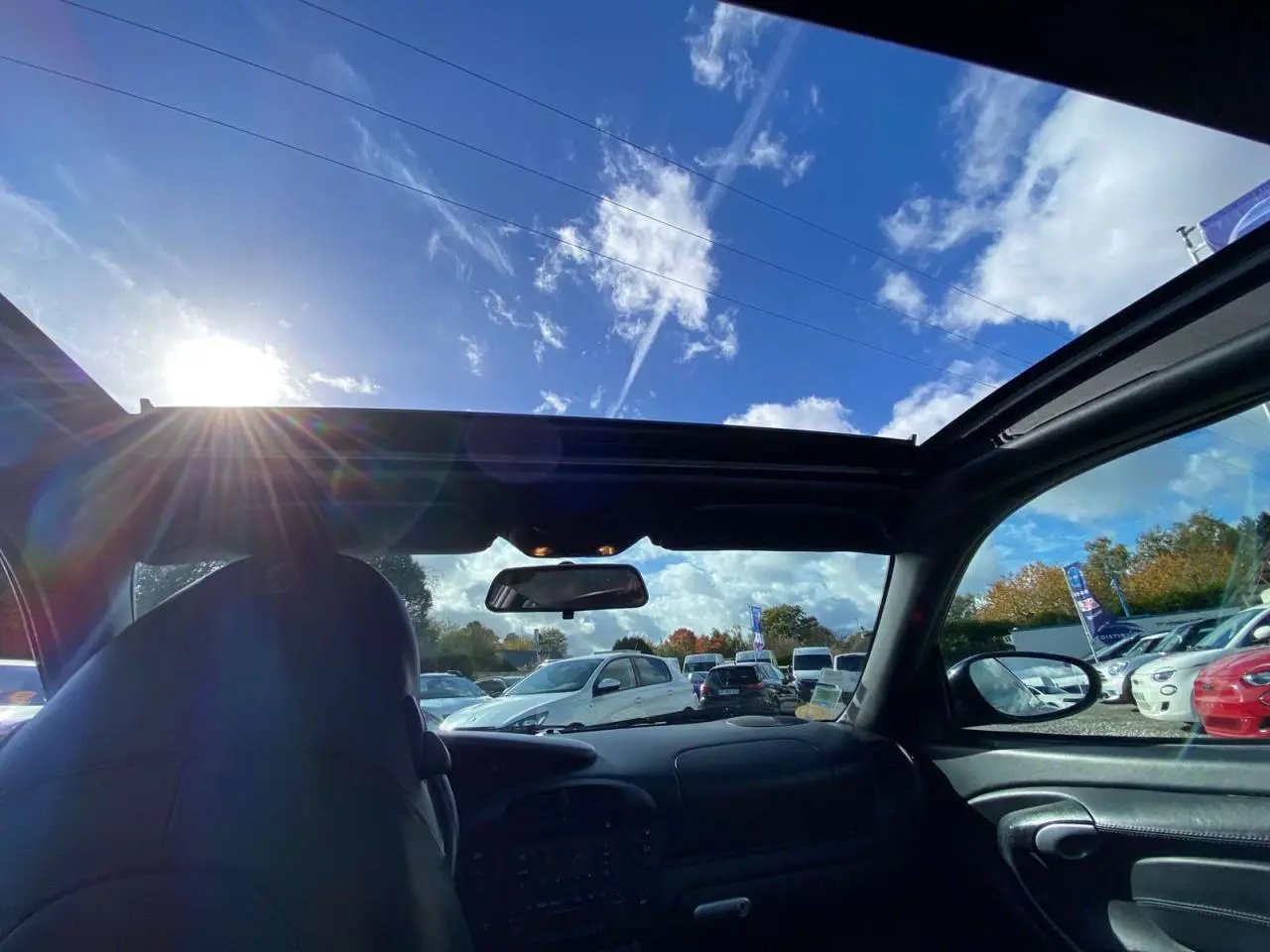 Vue intérieure avant d'une Porsche 911 Targa gris foncé de 2004, avec toit ouvert sous un ciel bleu lumineux.