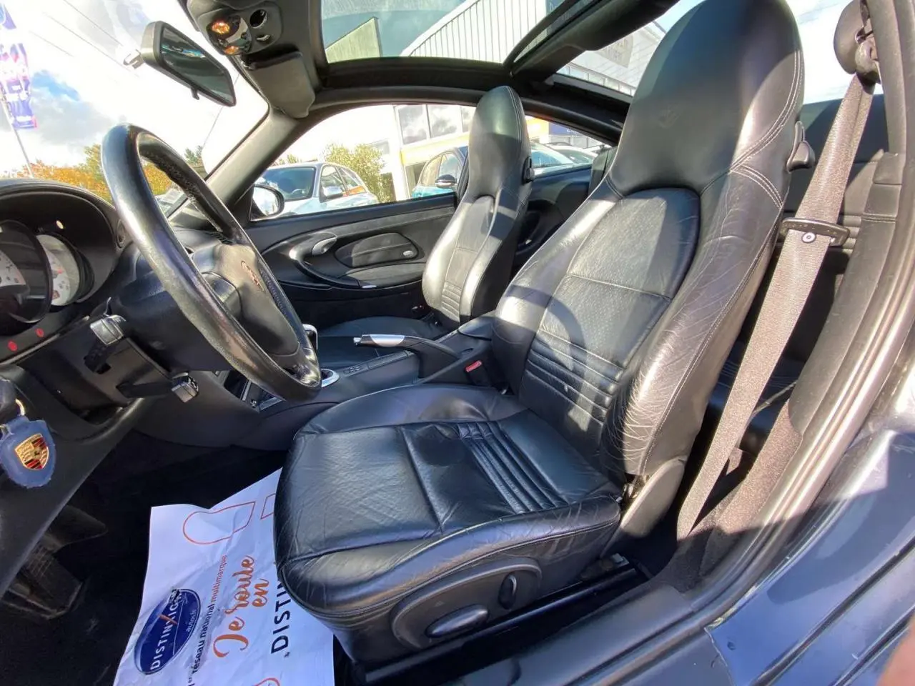 Intérieur côté conducteur d'une Porsche 911 Targa 2004 gris foncé, sièges cuir noir et volant sport visible.