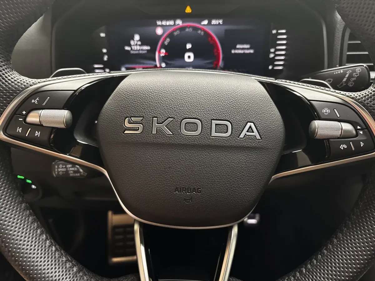 Gros plan sur le volant noir SKODA avec commandes intégrées et tableau de bord numérique en arrière-plan.