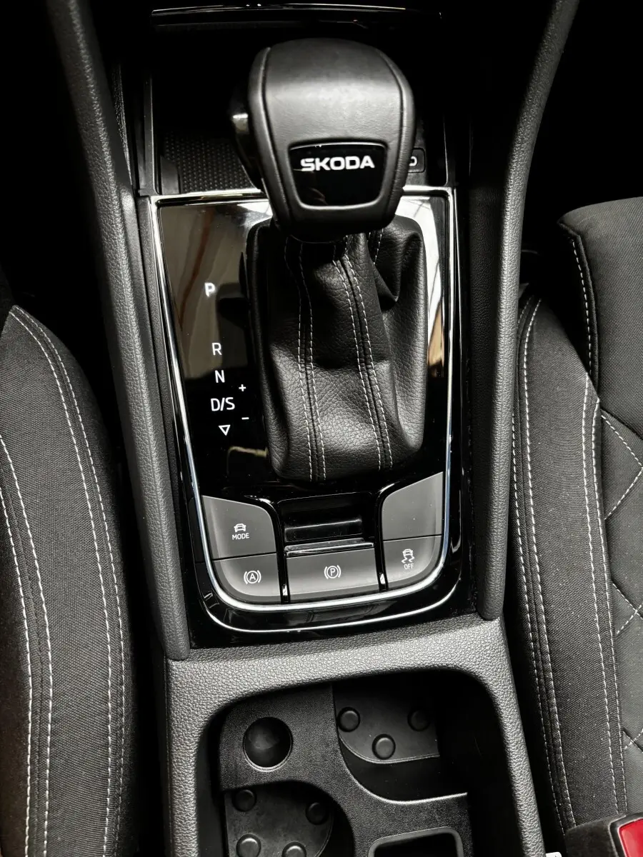 Gros plan sur le levier de vitesses automatique noir marqué SKODA, entouré des sièges et commandes centrales du Skoda Karoq.