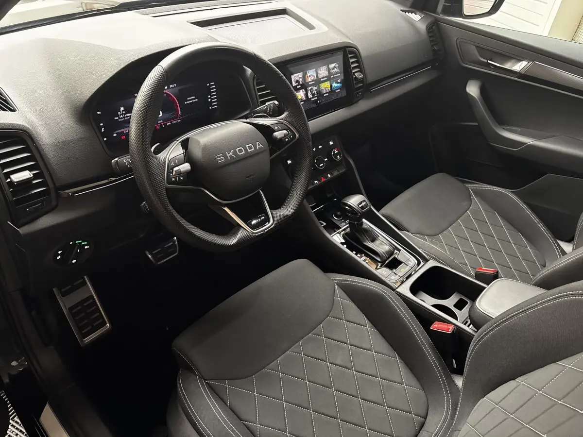 Vue intérieure côté conducteur du Skoda Karoq 2025 noir, avec volant cuir, sièges noirs matelassés et écran tactile central.