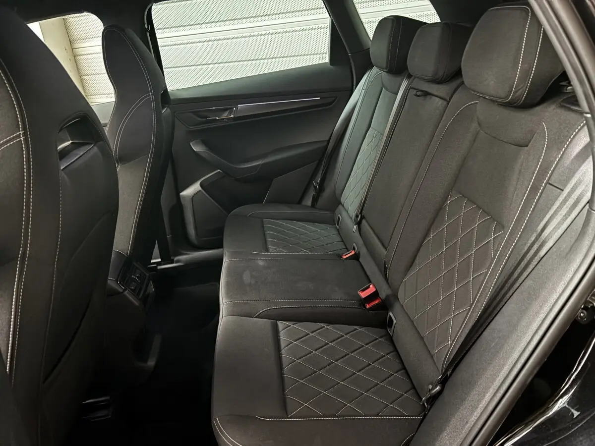 Vue côté droit de la banquette arrière noire du Skoda Karoq 2025 avec surpiqûres et ceintures rouges visibles.