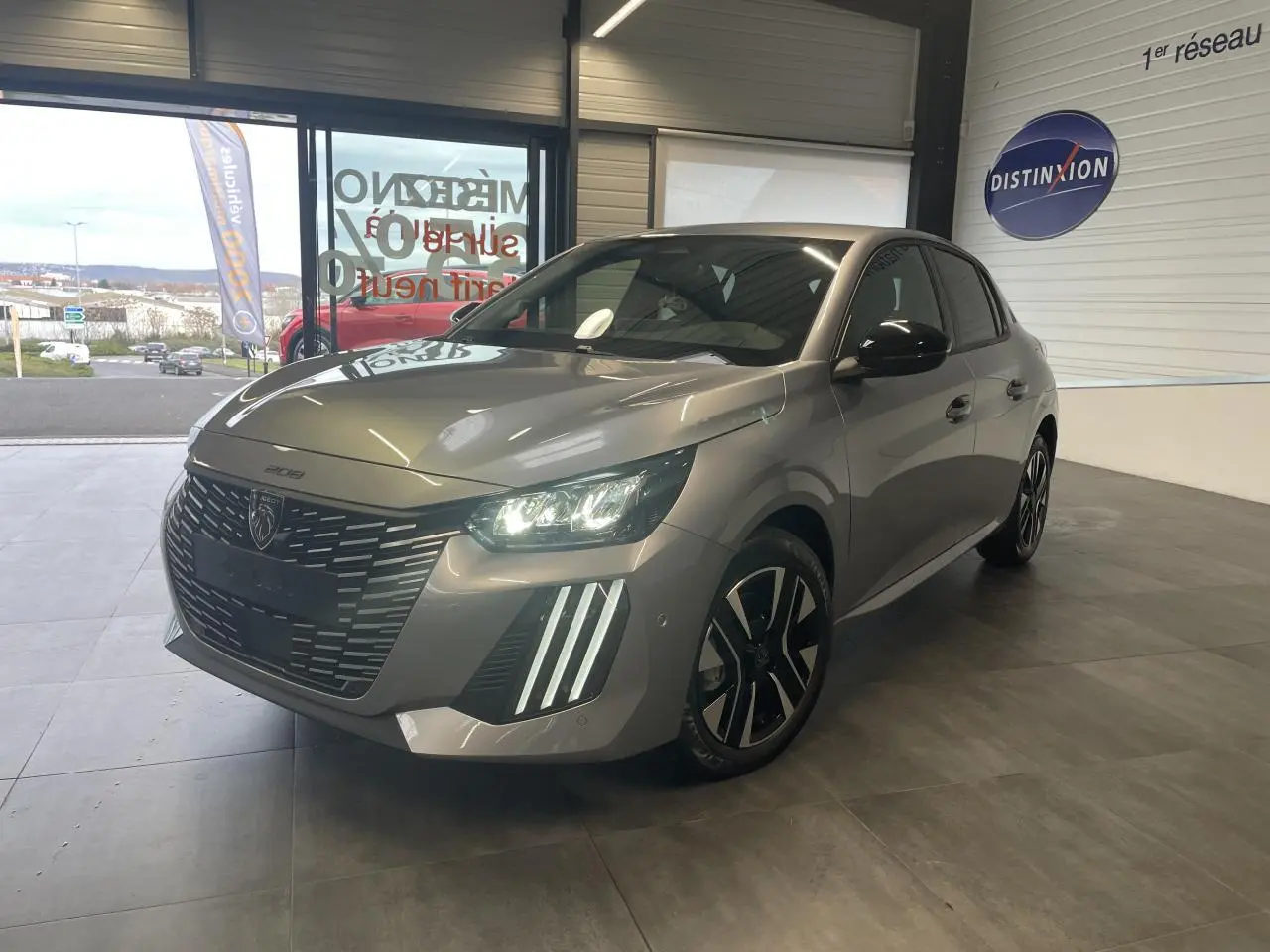 PEUGEOT 208 gris Artense en 3/4 avant droit, avec calandre noire et feux LED allumés dans un showroom.