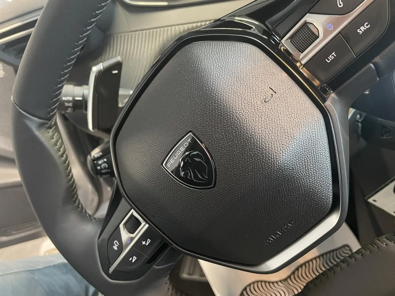 Gros plan sur le volant cuir noir du Peugeot 208 2025 avec logo lion et commandes intégrées.