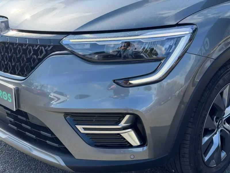 Gros plan sur l'avant droit du Renault Arkana gris métallisé 2025, mettant en valeur le phare LED et la calandre distinctive.