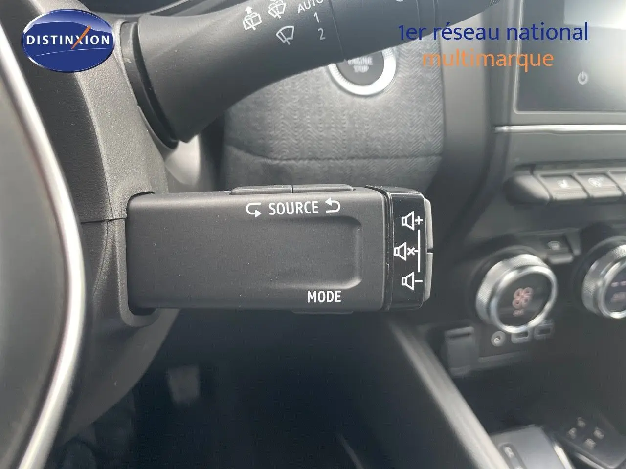 Commande multimédia au volant côté gauche de la Renault Clio TCe 90ch Techno 2025 avec tableau de bord noir et commandes climatiques visibles.