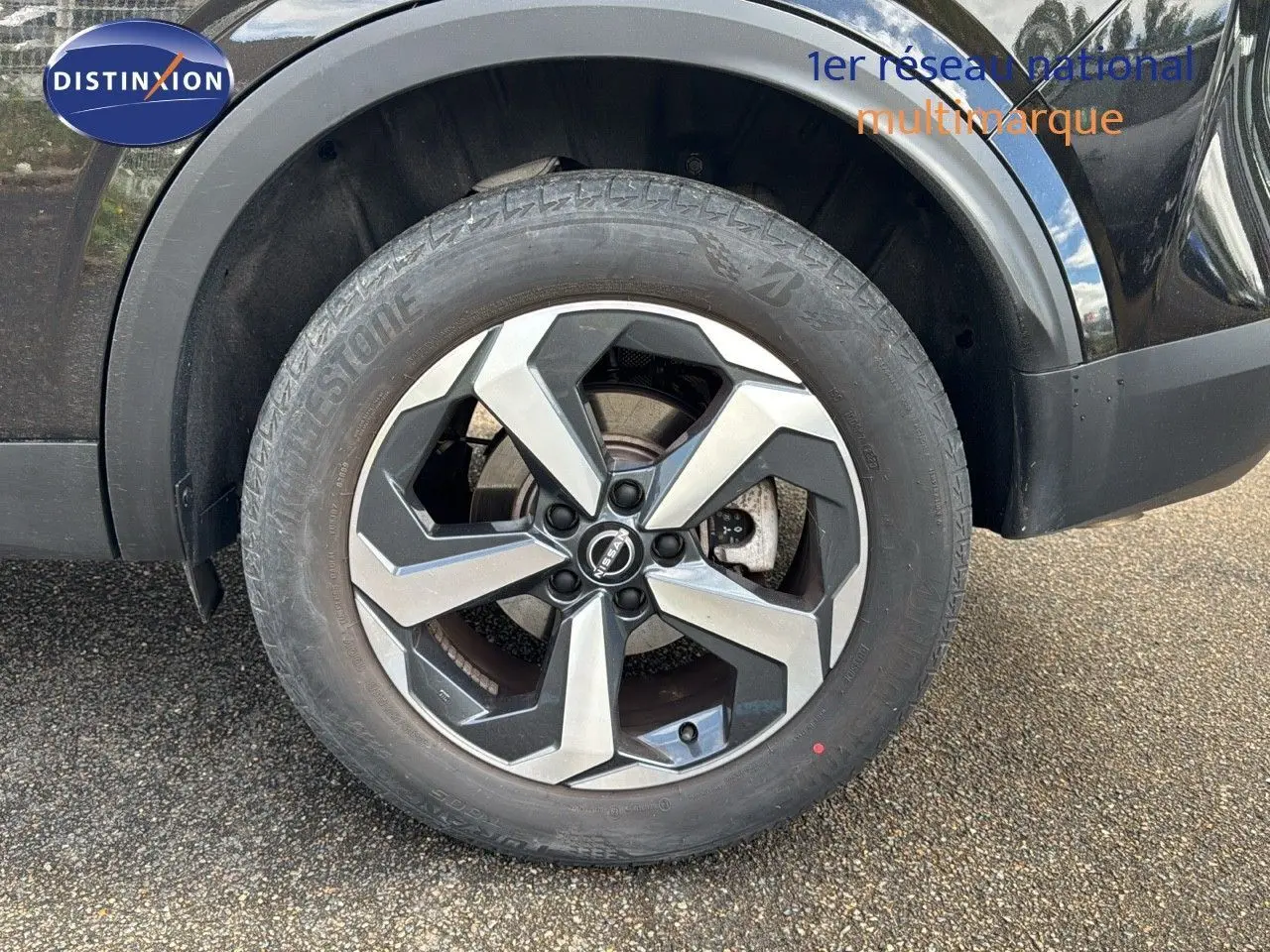 Gros plan sur la roue avant gauche du Nissan Qashqai noir 2024, mettant en valeur la jante alliage bicolore au design moderne.