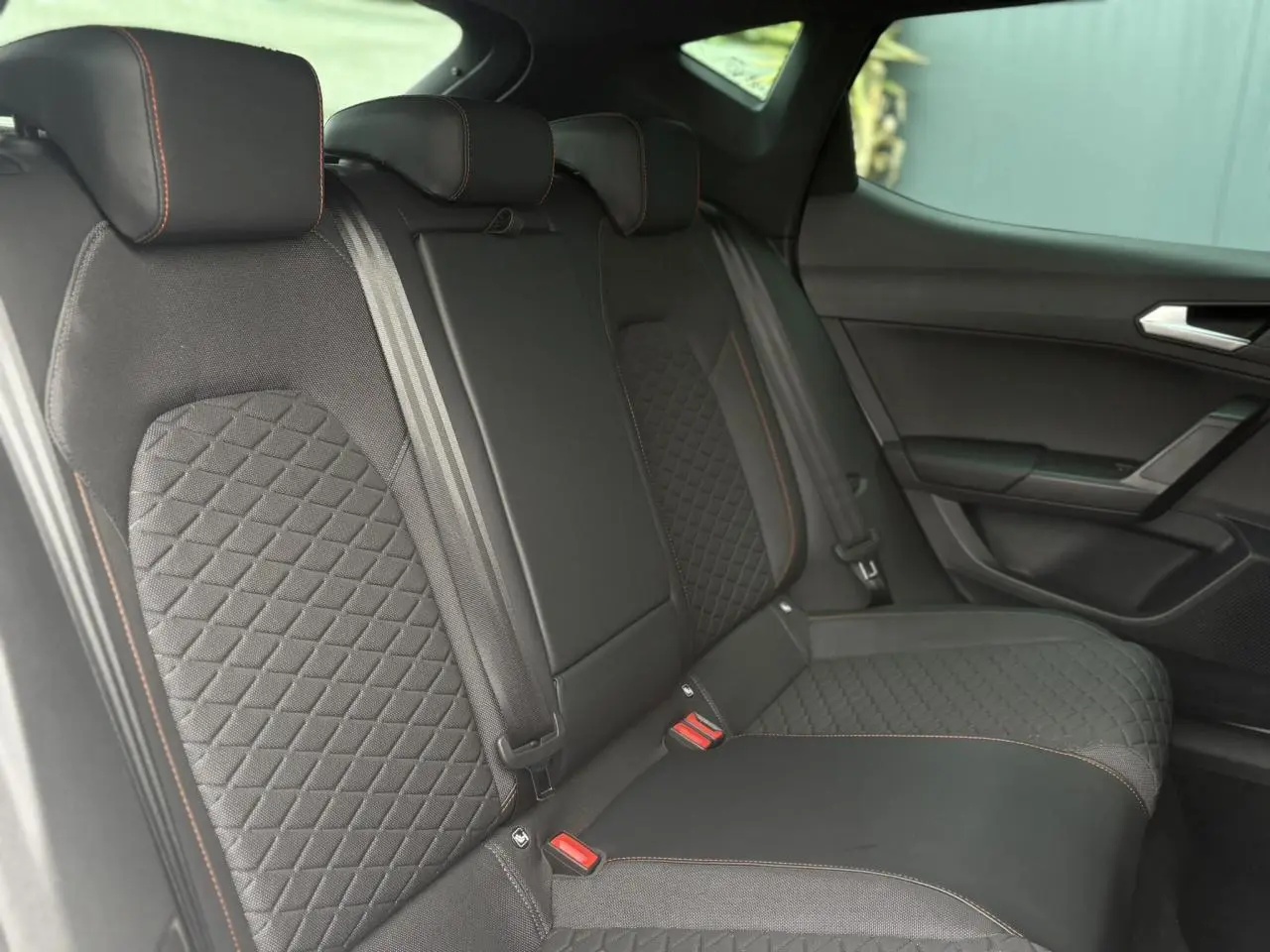 Vue intérieure des sièges arrière noirs avec surpiqûres orange de la SEAT LEON 2024 côté droit.