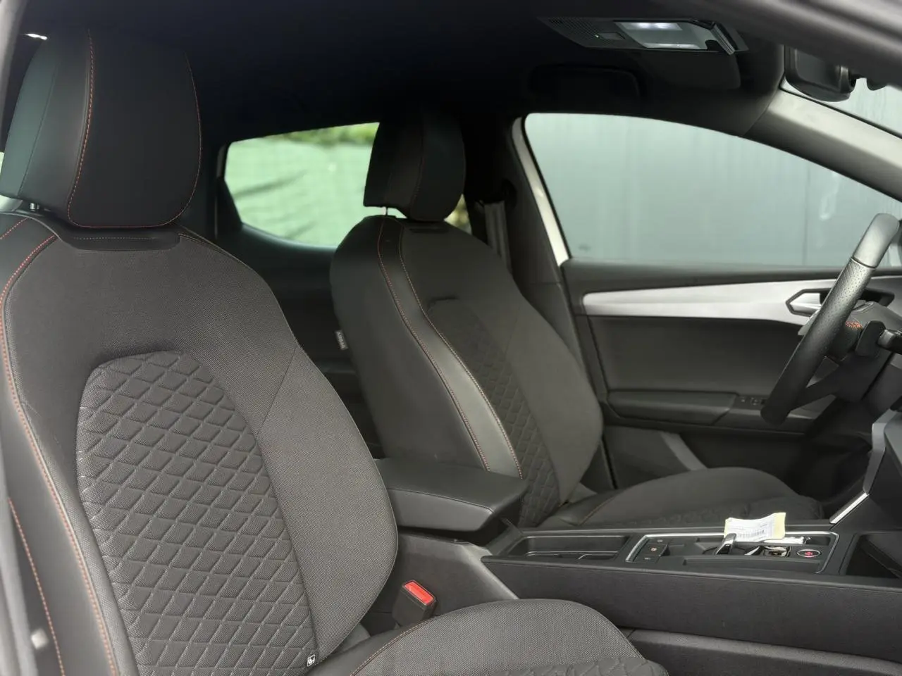 Vue intérieure côté droit du SEAT LEON 2024 avec sièges tissu noir à surpiqûres orange et console centrale moderne.