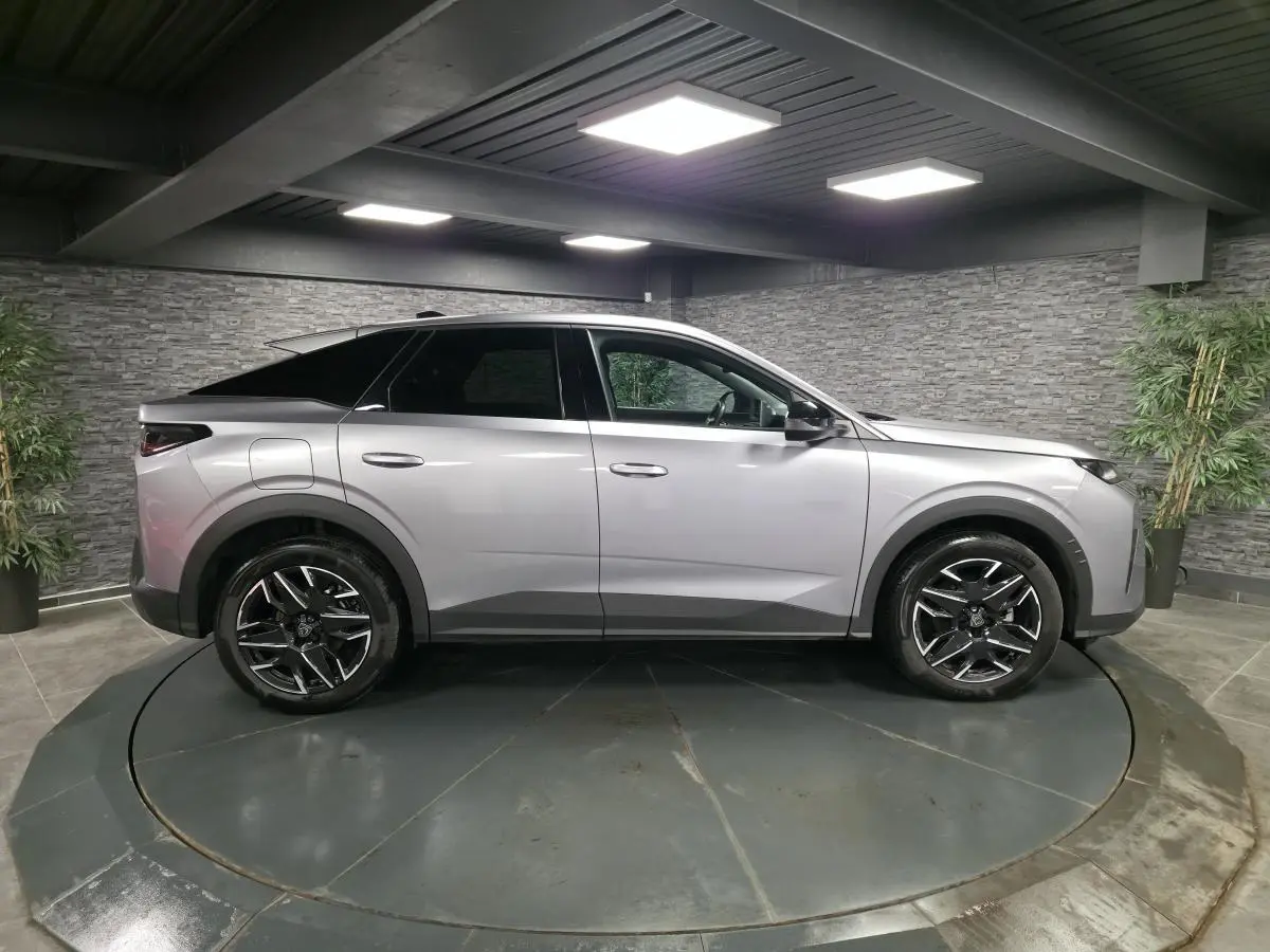 Vue latérale droite d’un Peugeot 3008 gris métallisé 2025 avec jantes alliage noires et toit noir dans un showroom.