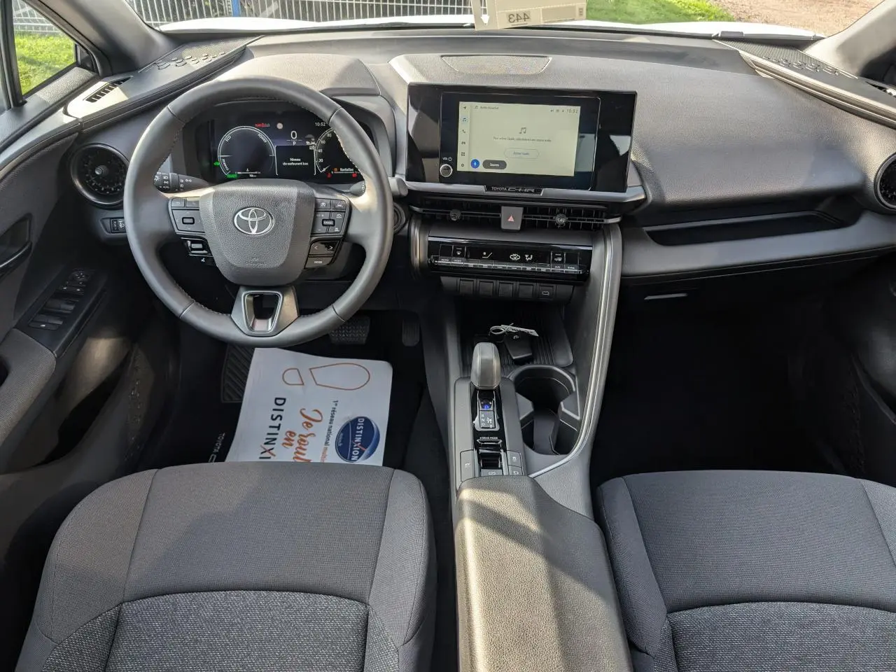 Vue intérieure avant du Toyota C-HR 2024 hybride, tableau de bord avec écran tactile 8 pouces et volant multifonctions.