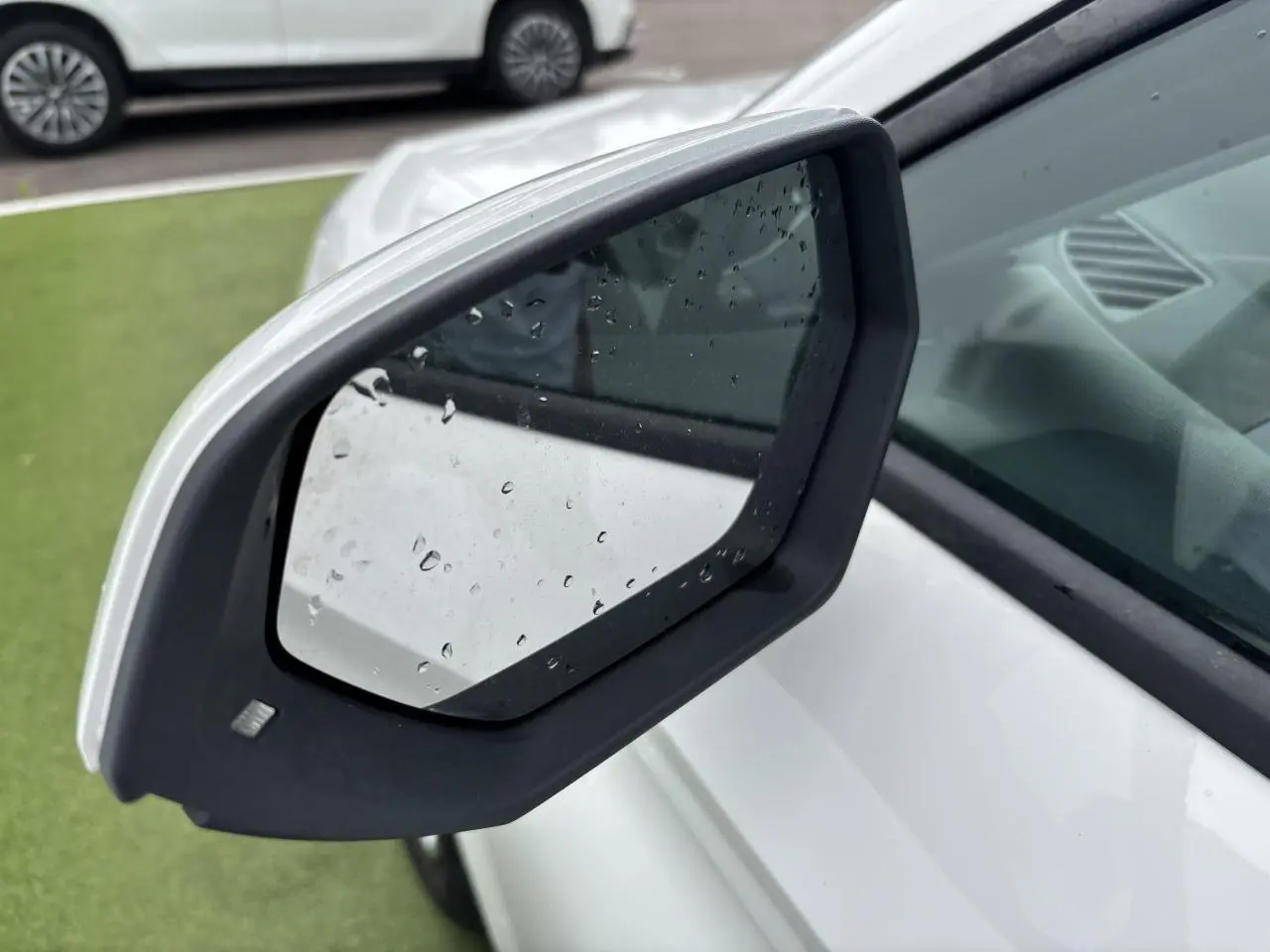 Rétroviseur côté gauche blanc de la SEAT LEON IV 1.5 TSI 130CH STYLE PACK 2024 avec gouttes de pluie visibles.