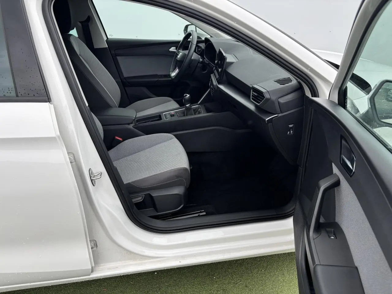 Intérieur côté conducteur d'une SEAT Leon blanche 2024, montrant sièges gris, volant cuir et tableau de bord moderne.