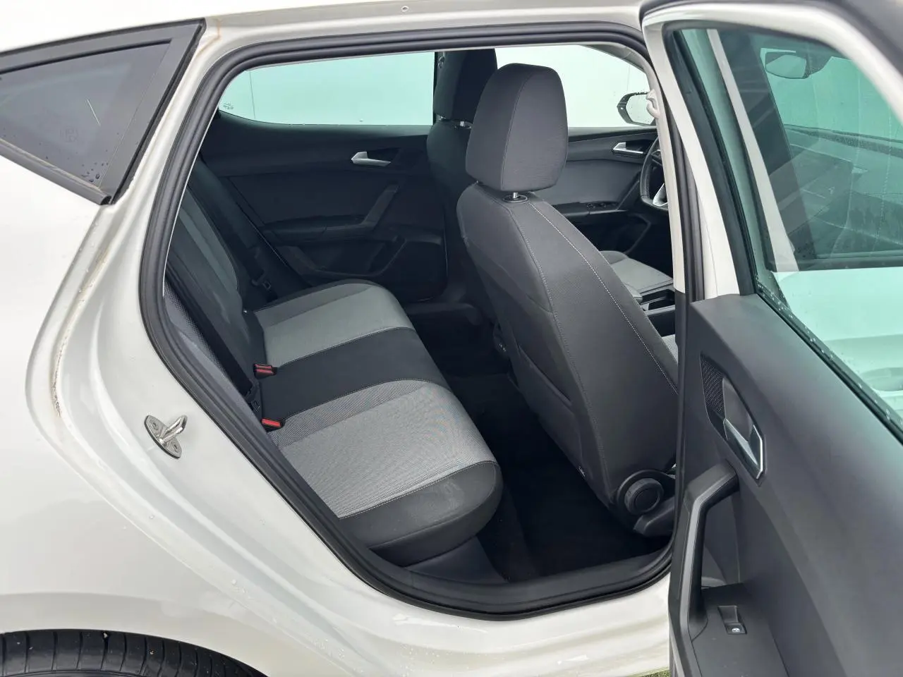 Vue intérieure côté gauche arrière d'une SEAT LEON blanche 2024, montrant les sièges arrière bicolores et la porte ouverte.
