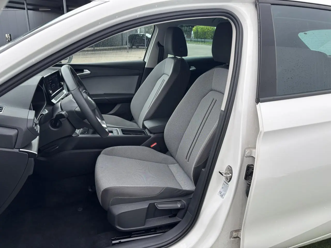 Intérieur côté conducteur d'une SEAT LEON blanche 2024, montrant les sièges gris et le volant multifonction cuir.