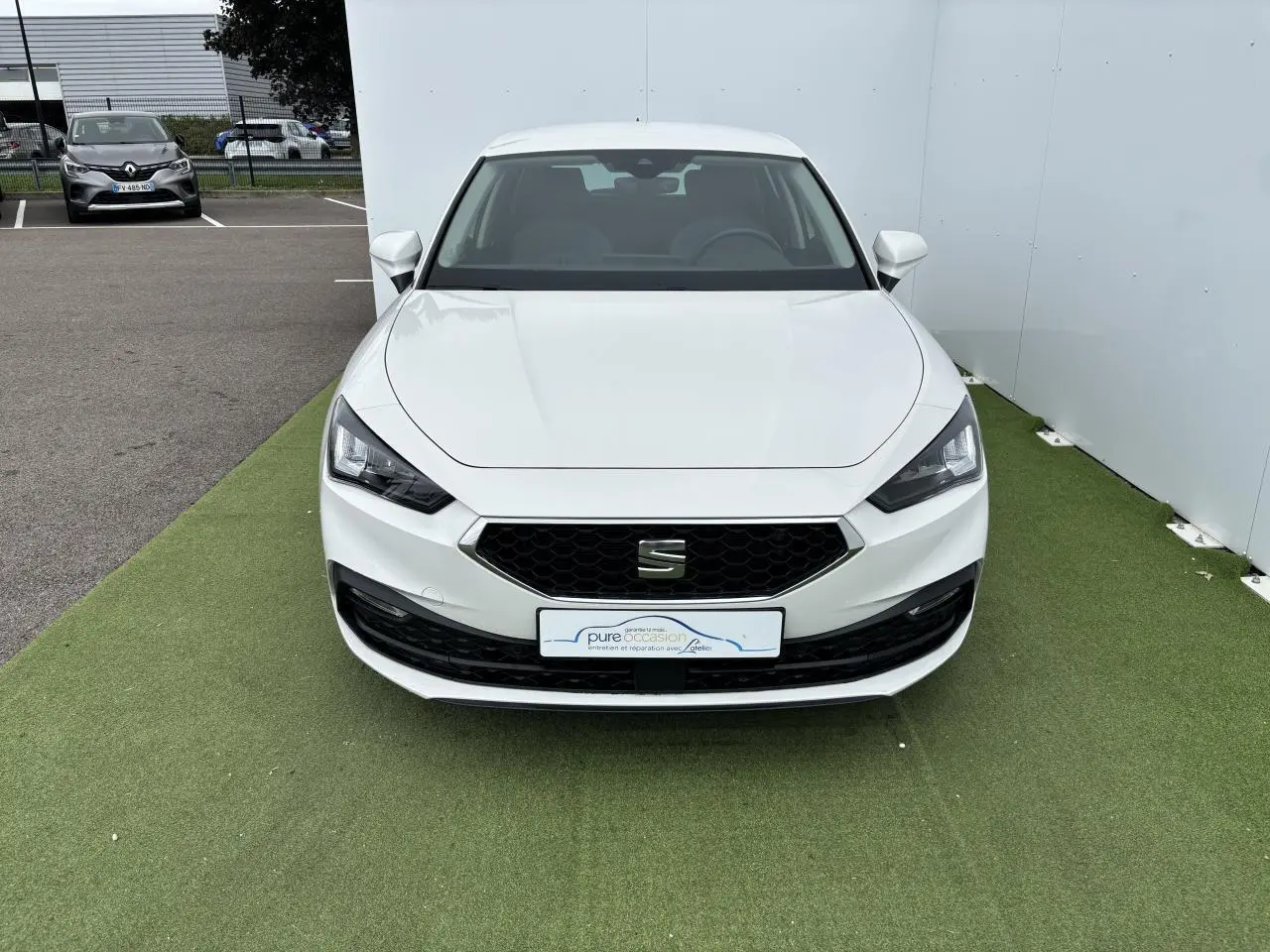 Vue frontale d'une SEAT Leon IV blanche avec calandre noire hexagonale et projecteurs Full LED, stationnée sur sol vert.