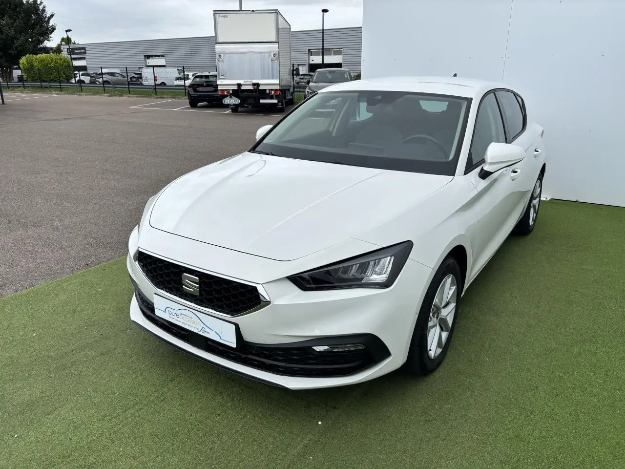 SEAT Leon IV blanche vue en 3/4 avant droit, avec calandre noire et jantes alliage 16 pouces sur fond vert.