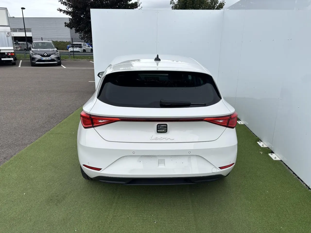 Vue arrière d'une SEAT Leon blanche 2024 garée sur sol vert avec feux arrière LED et lunette arrière teintée.