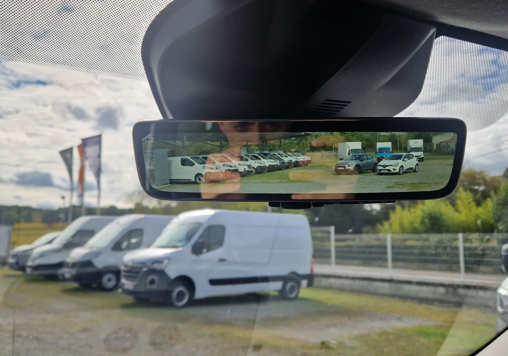 Vue depuis l'intérieur sur le rétroviseur numérique montrant plusieurs véhicules utilitaires blancs en extérieur.