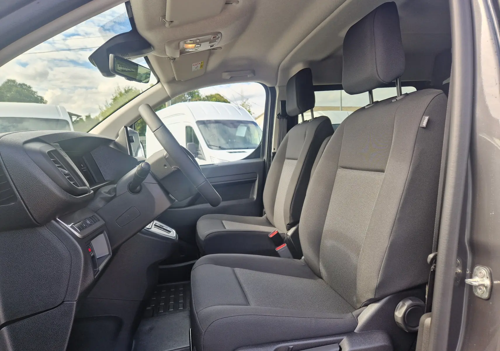 Vue intérieure côté conducteur du Citroën Jumpy XL gris titane, montrant les sièges avant et le tableau de bord.