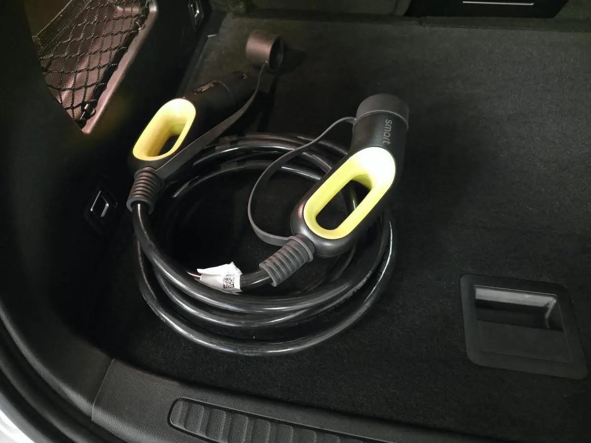 Gros plan sur le câble de recharge électrique noir avec poignées jaunes dans le coffre d'une Smart #1 blanche.