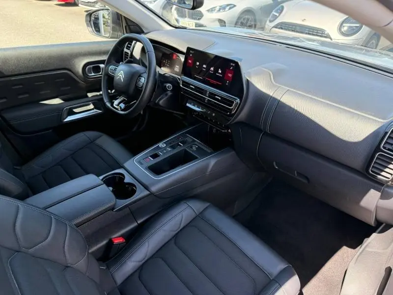 Intérieur du Citroën C5 Aircross 2024 vu côté conducteur, avec tableau de bord moderne et sièges tissu gris effet cuir.