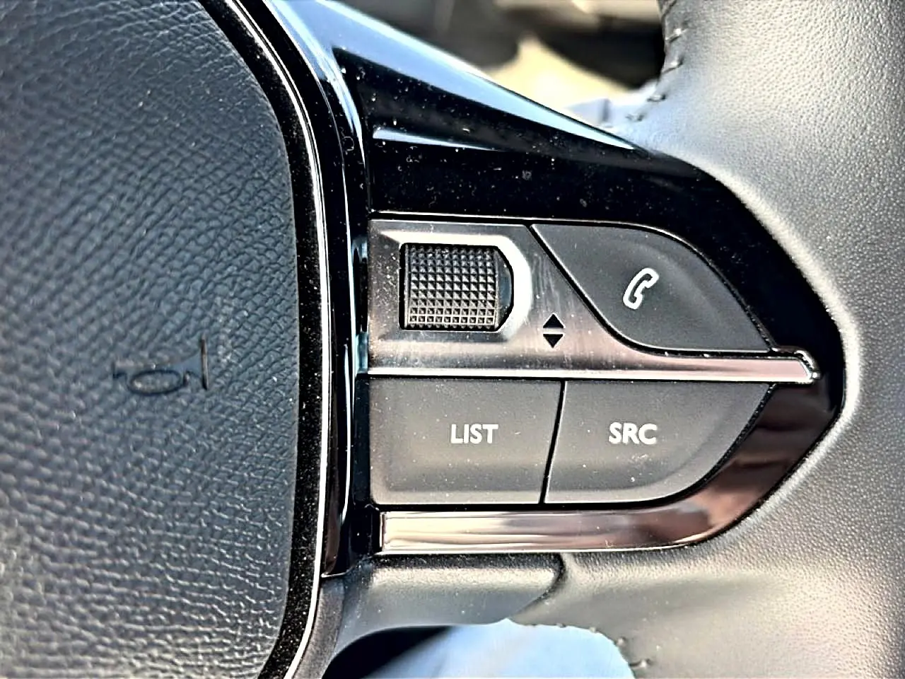 Gros plan sur les commandes gauche du volant noir du Peugeot 2008 gris, boutons list, src et téléphone visibles.