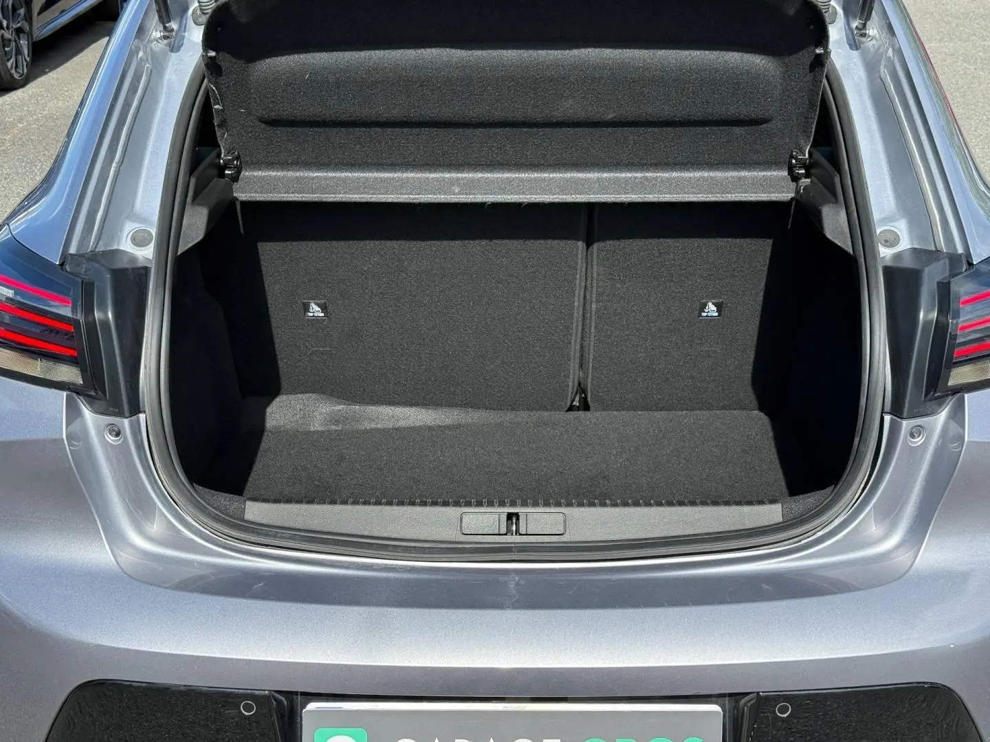 Coffre ouvert vu de l'arrière d'une Peugeot 208 gris Artense, montrant l'espace de chargement vide et les feux arrière LED.