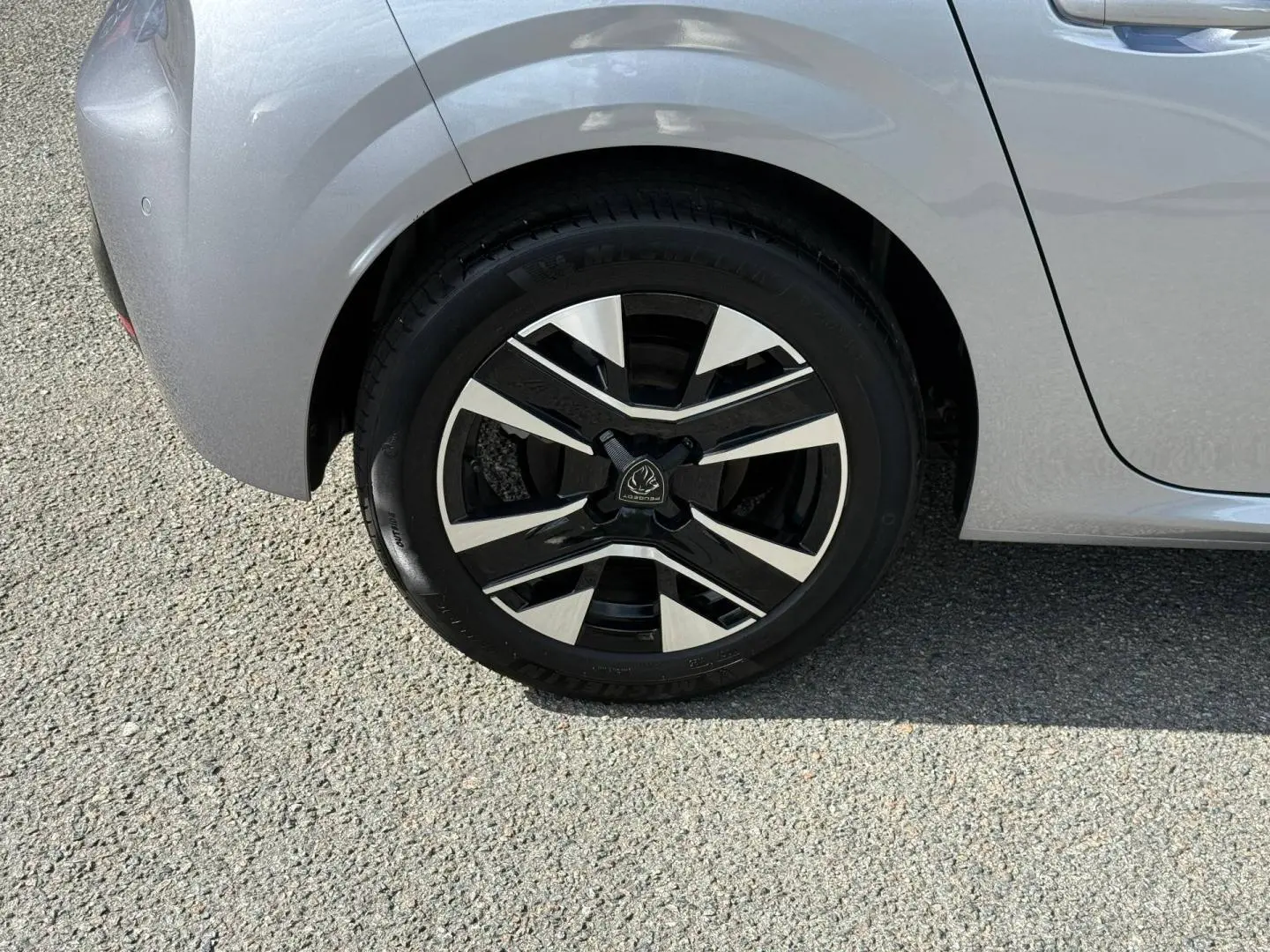 Gros plan sur la roue arrière gauche de la Peugeot 208 gris Artense avec jante alu bicolore au design moderne.